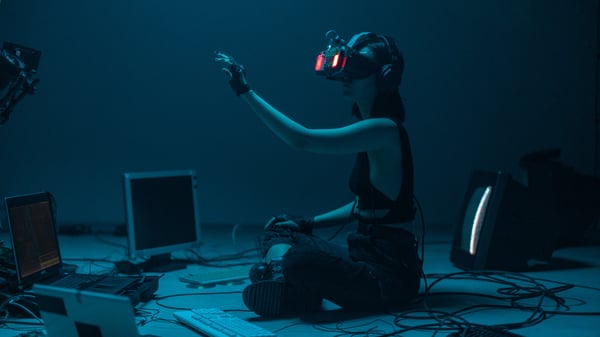 A woman sittingin between computer monitors wearing VR glasses and interacting with the digital content possibly AI.